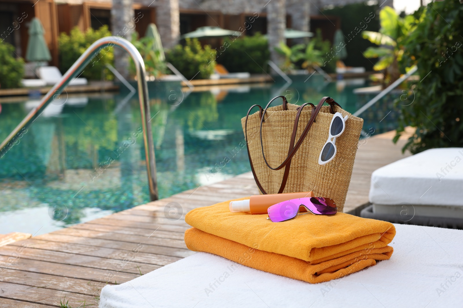 Photo of Wicker bag with beach accessories on sunbed near outdoor swimming pool, space for text. Luxury resort