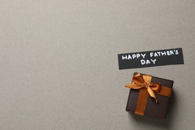 Card with phrase HAPPY FATHER'S DAY and gift box on light grey background, flat lay. Space for text