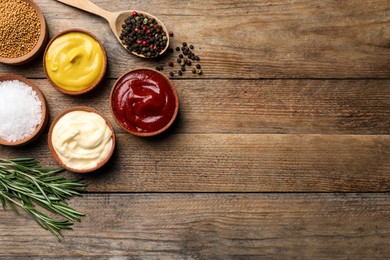 Photo of Flat lay composition with ketchup, mustard, mayonnaise and ingredients on wooden table, space for text