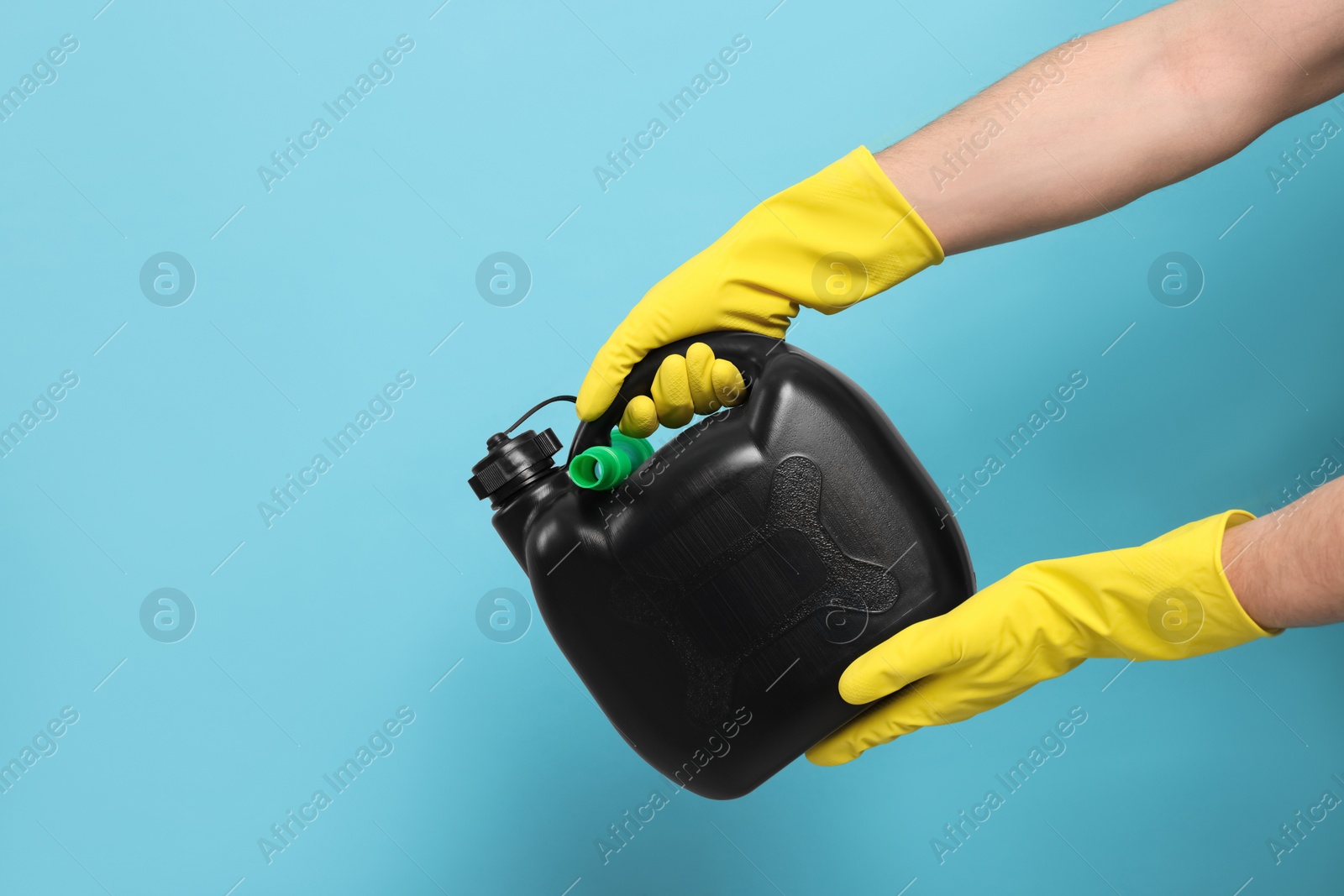 Photo of Man in rubber gloves holding black canister on light blue background, closeup. Space for text