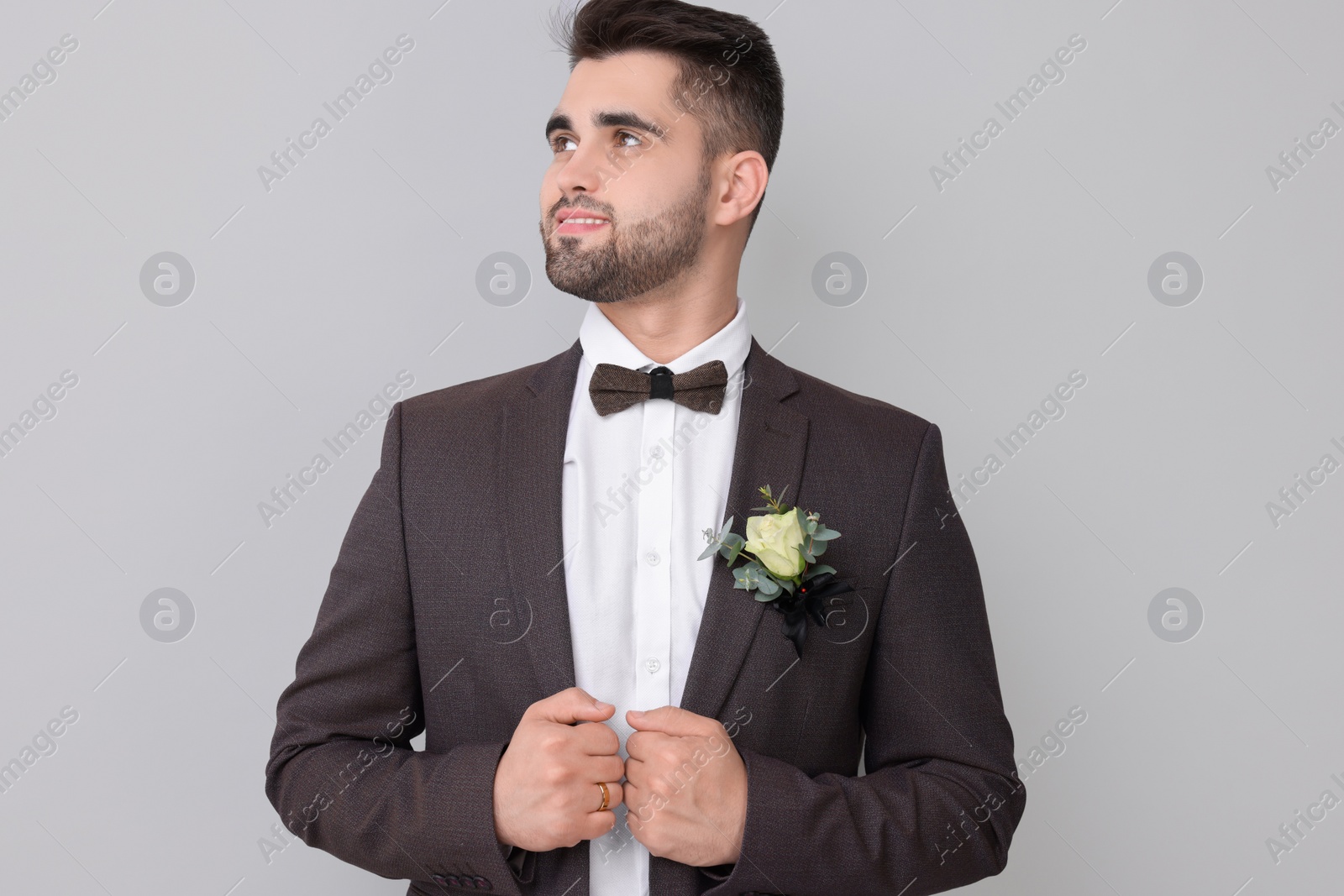 Photo of Handsome young groom with boutonniere on light grey background. Wedding accessory