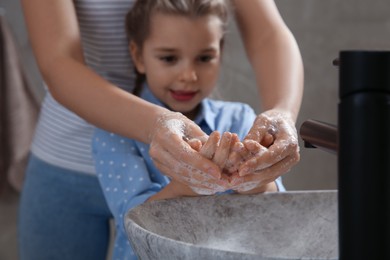 Mother and daughter washing hands with liquid soap together in bathroom, closeup