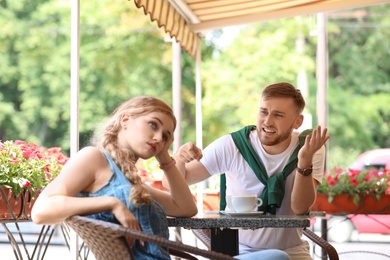 Photo of Young couple arguing while sitting in cafe, outdoors. Problems in relationship