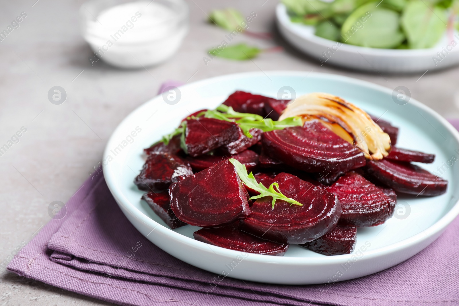 Photo of Roasted beetroot slices with onion and arugula on light grey table, closeup