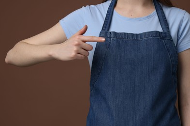 Woman pointing at kitchen apron on brown background, closeup. Mockup for design