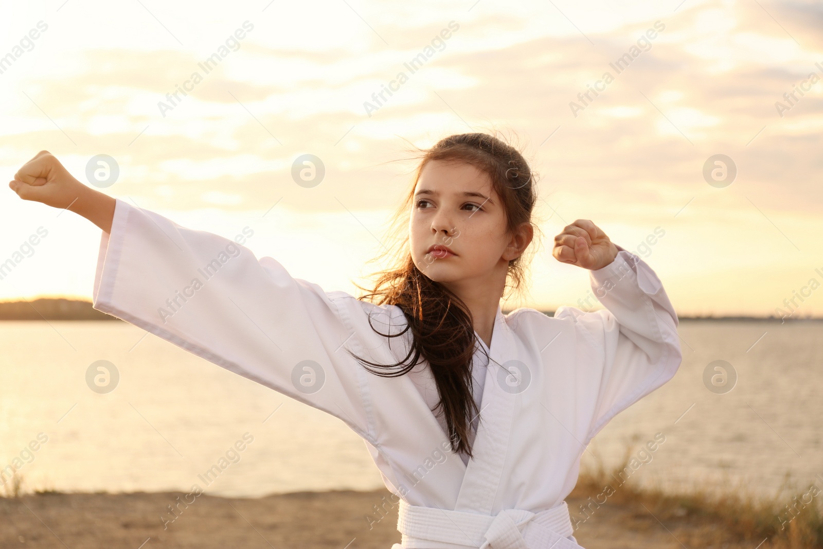 Photo of Cute little girl in kimono practicing karate near river at sunset