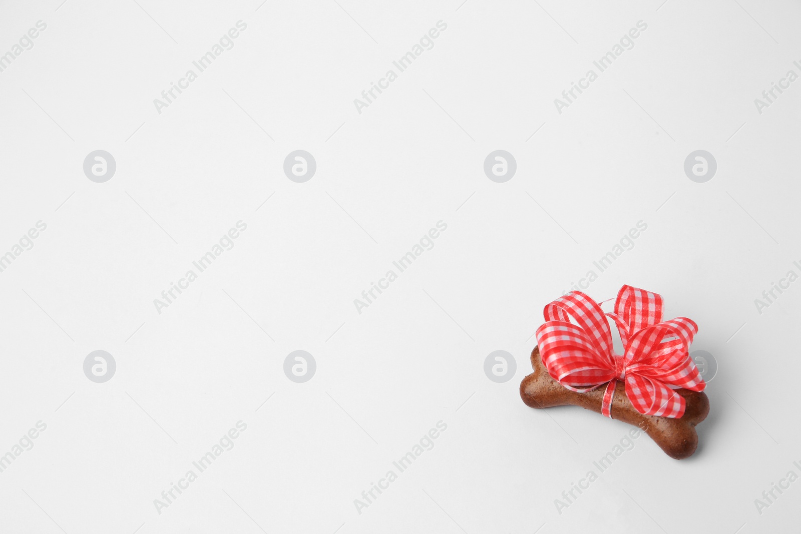 Photo of Bone shaped dog cookie with red bow on white background, top view. Space for text