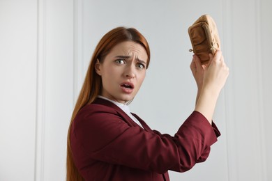 Confused woman with empty wallet near white wall