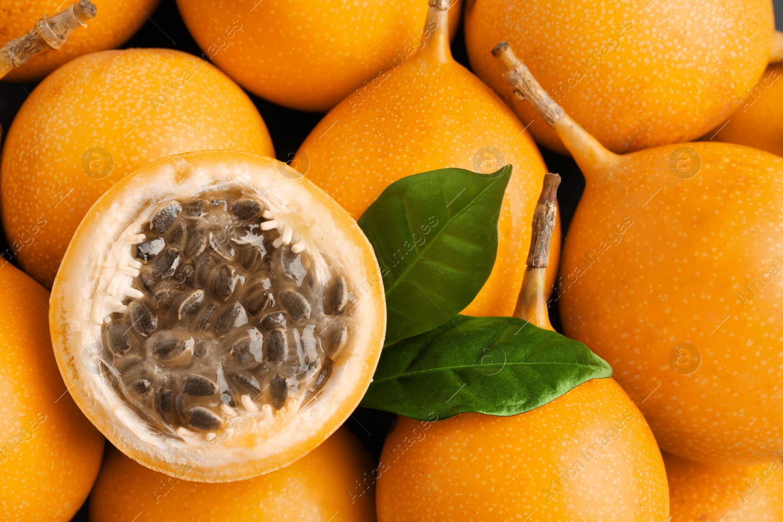 Photo of Delicious whole and cut granadillas with leaves as background, top view