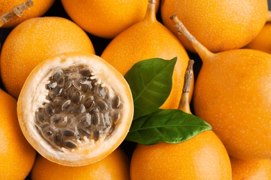 Photo of Delicious whole and cut granadillas with leaves as background, top view