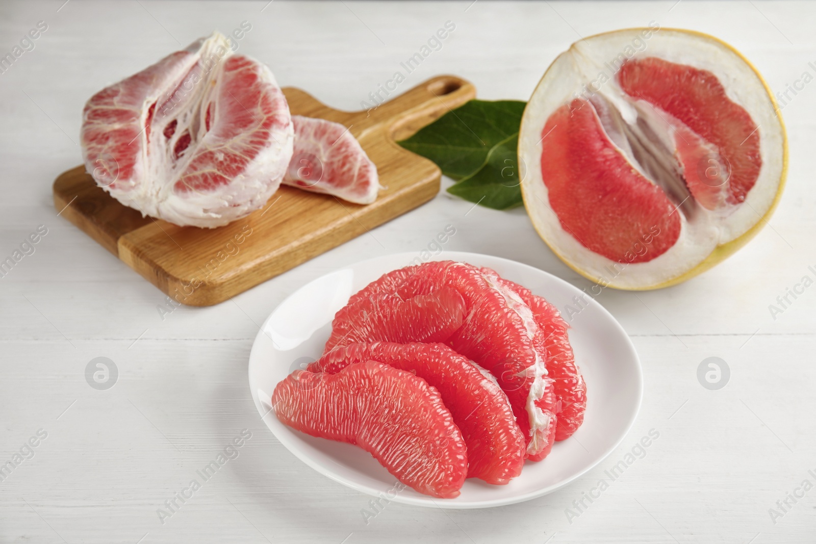 Photo of Peeled red pomelo slices on white wooden table