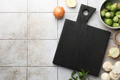 Photo of Flat lay composition with black cutting board and products on light tiled table. Space for text
