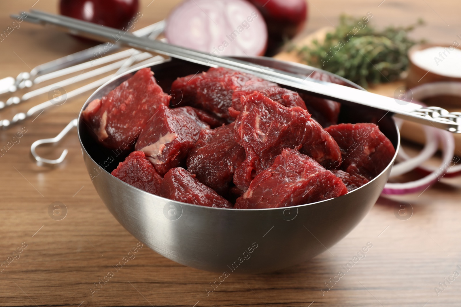 Photo of Metal skewers and bowl with raw meat on wooden table