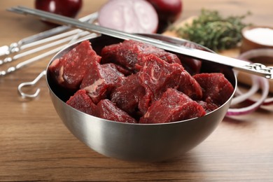 Metal skewers and bowl with raw meat on wooden table