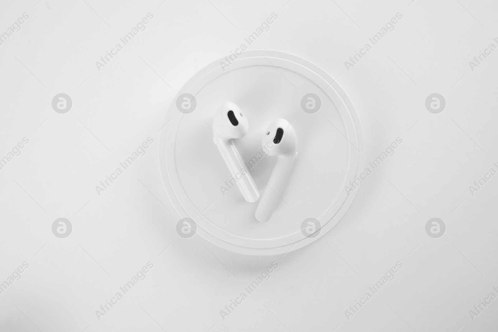 Photo of Earphones charging with wireless pad isolated on white, top view