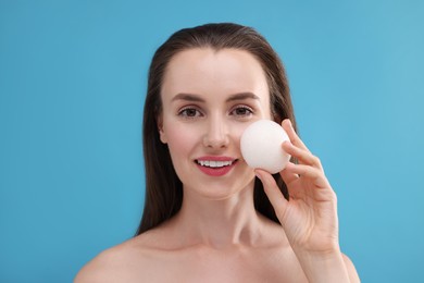 Photo of Happy young woman holding face sponge on light blue background