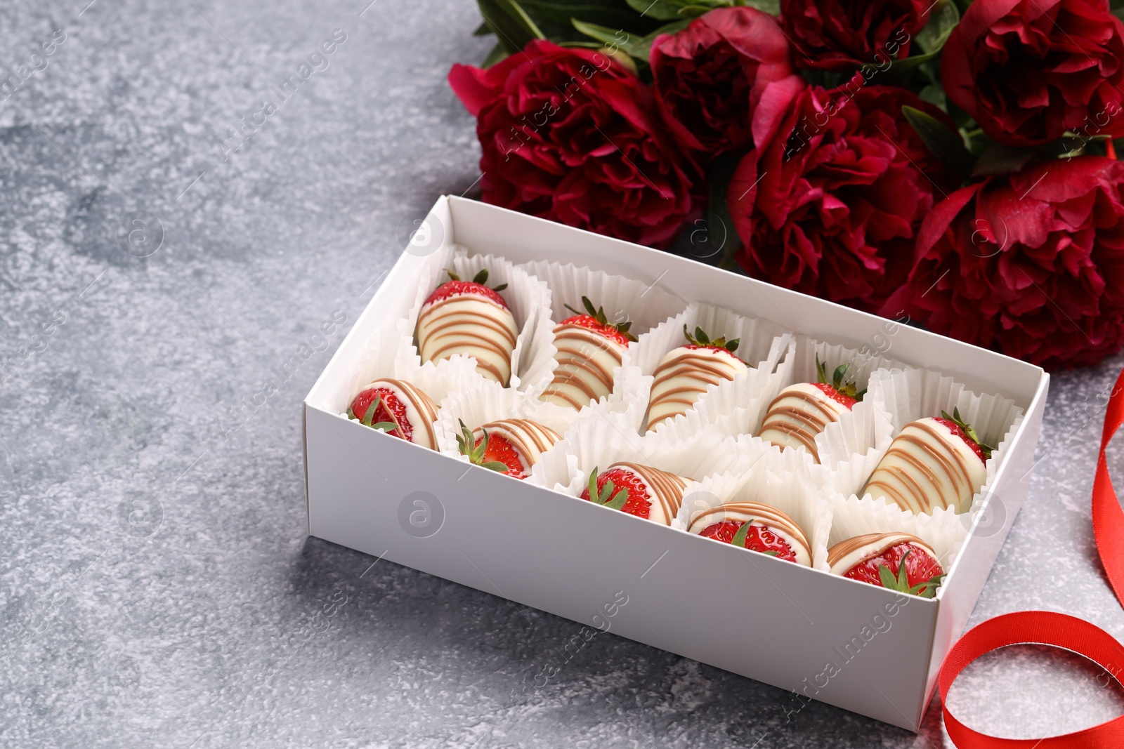 Photo of Delicious chocolate covered strawberries in box and flowers on light grey table. Space for text