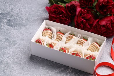 Delicious chocolate covered strawberries in box and flowers on light grey table. Space for text