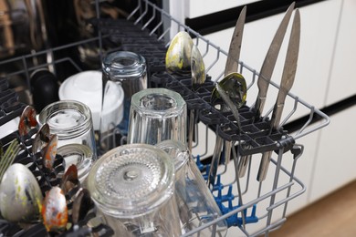 Photo of Open modern dishwasher with dirty tableware in kitchen, closeup