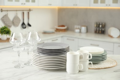 Clean plates, cups and glasses on white marble table in kitchen