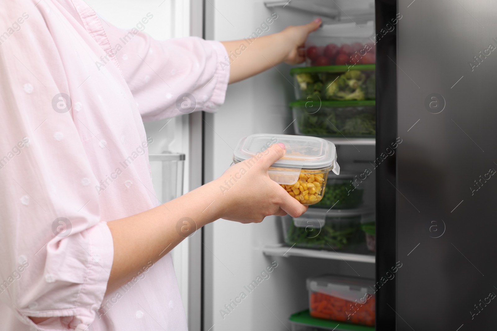 Photo of Woman putting container with tasty corn kernels into fridge, closeup. Food storage