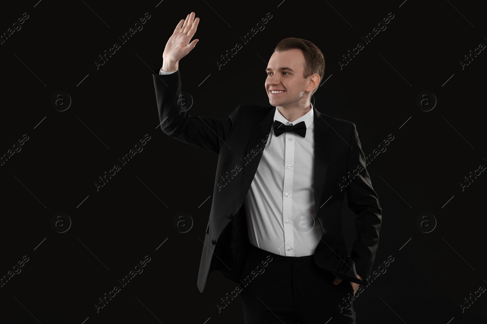 Photo of Handsome young man in stylish suit greeting someone on black background