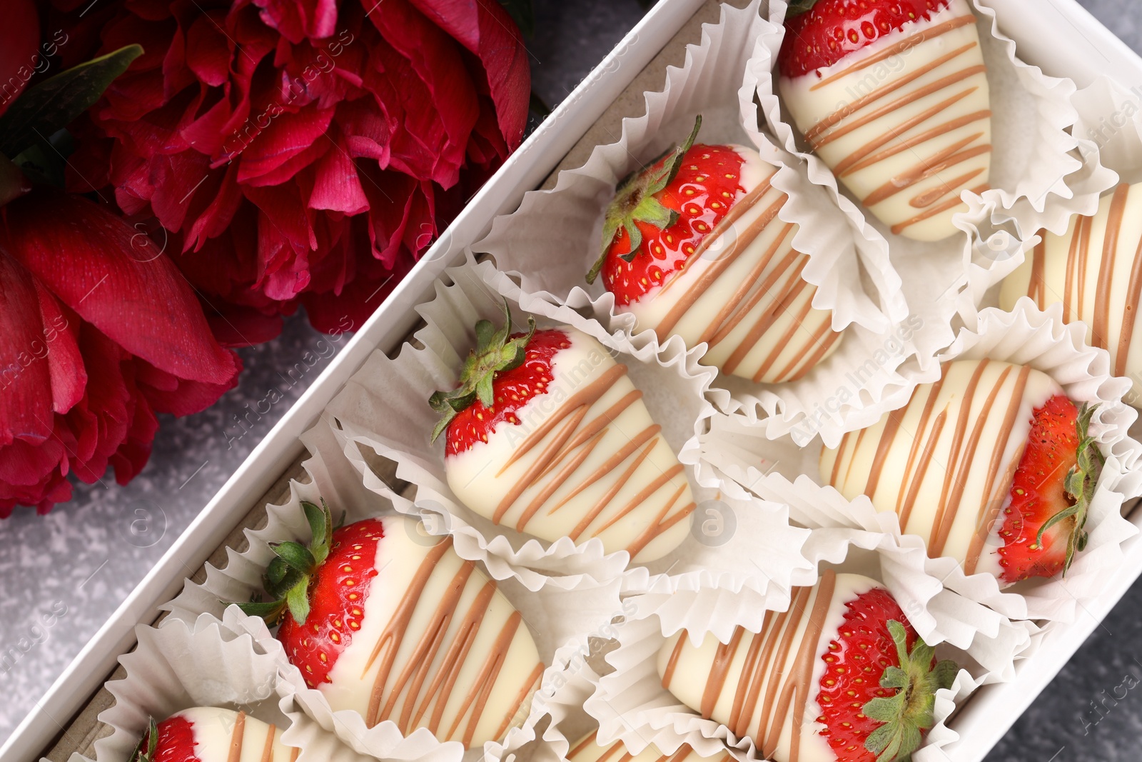 Photo of Delicious chocolate covered strawberries in box and flowers on light grey table, flat lay