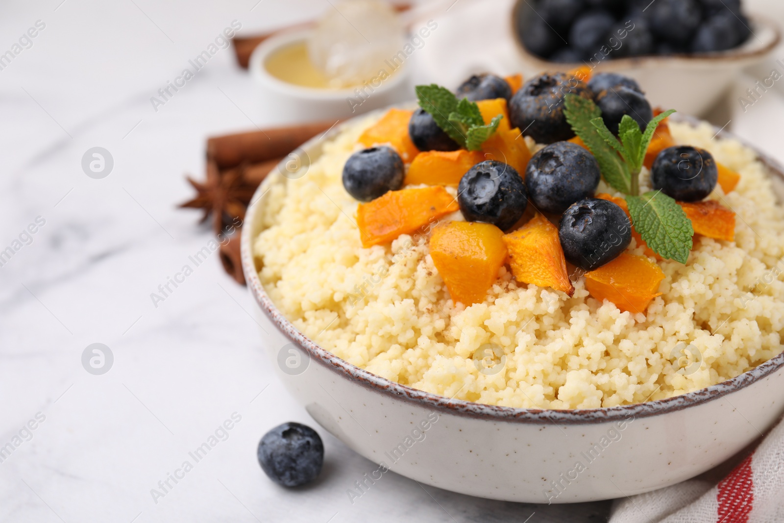Photo of Bowl of tasty couscous with blueberries, pumpkin and mint on white table, closeup. Space for text