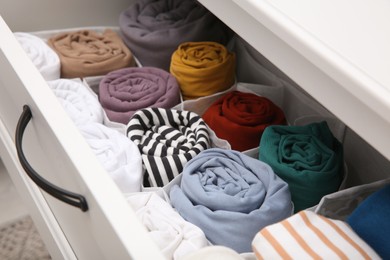 Open drawer with folded clothes indoors, closeup. Vertical storage