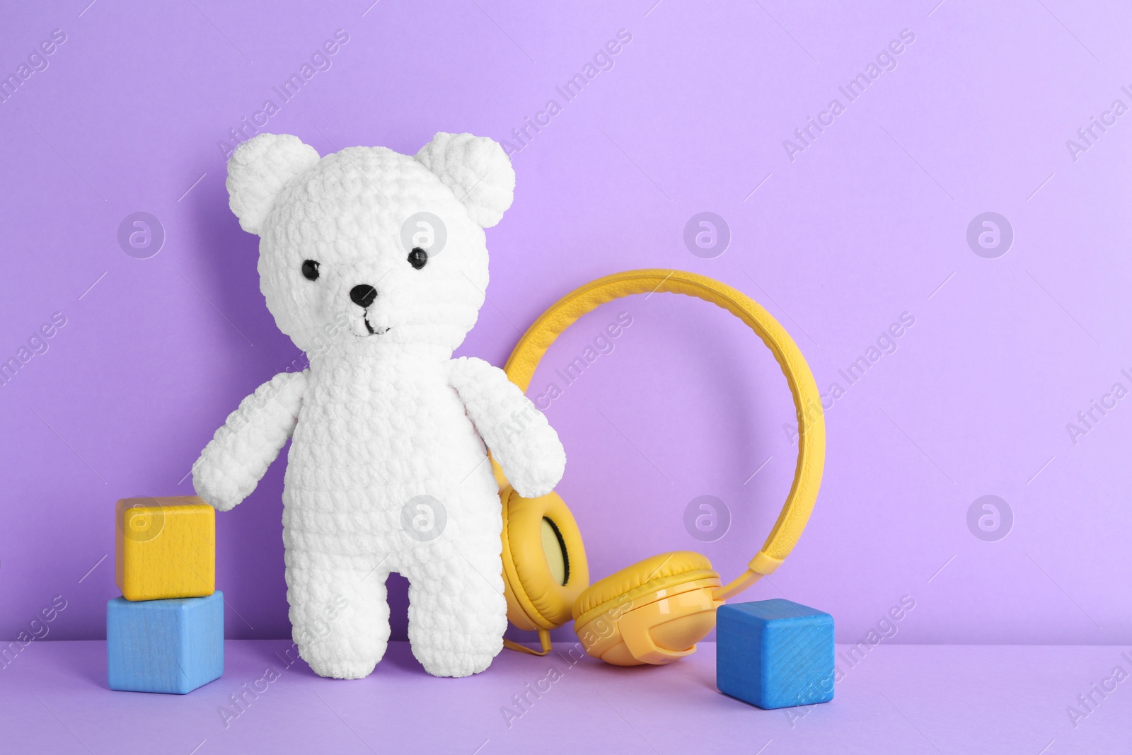 Photo of Baby songs. Toy bear, headphones and cubes on violet background