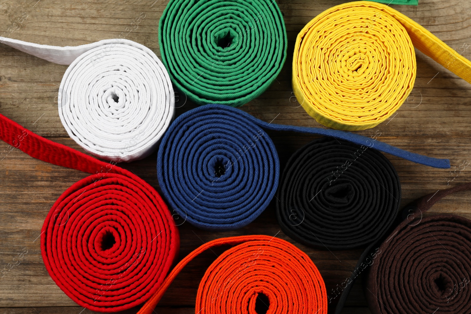 Photo of Colorful karate belts on wooden background, flat lay