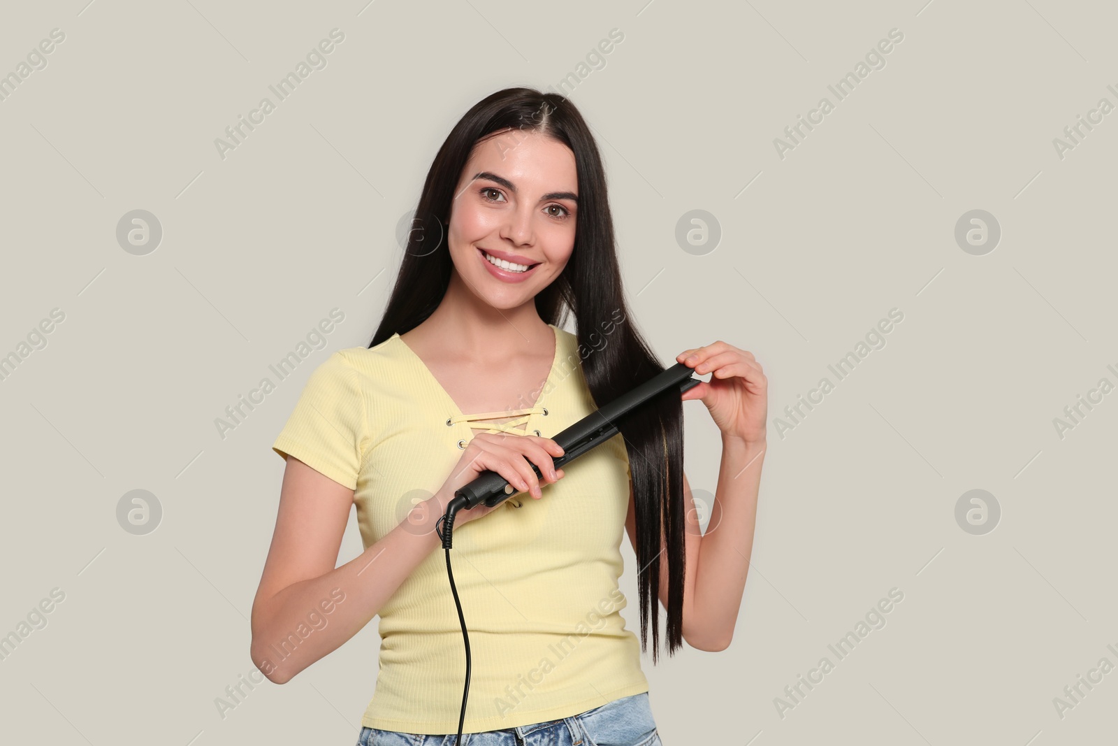 Photo of Beautiful happy woman using hair iron on light grey background