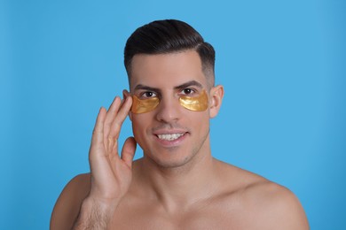 Man applying golden under eye patch on light blue background