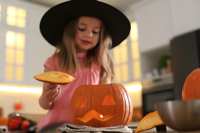 Photo of Little girl with pumpkin jack o'lantern at table in kitchen. Halloween celebration