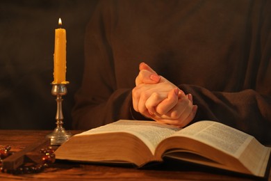 Photo of Woman praying at table with burning candle and Bible, closeup