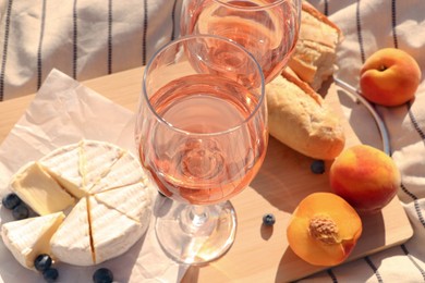 Photo of Glasses of delicious rose wine and food on white picnic blanket