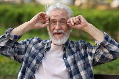 Portrait of happy grandpa with glasses on bench in park