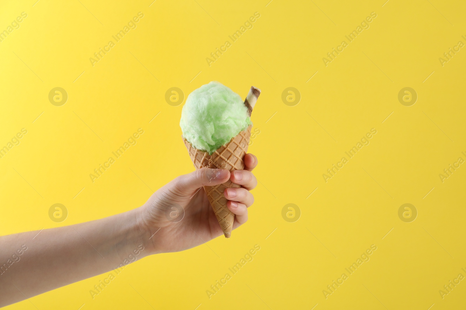 Photo of Woman holding waffle cone with cotton candy on yellow background, closeup