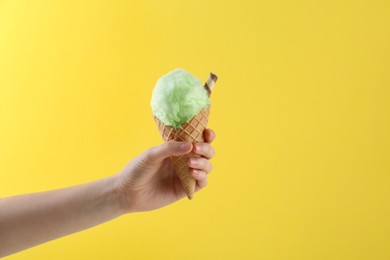 Woman holding waffle cone with cotton candy on yellow background, closeup