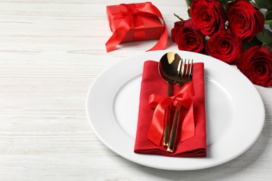 Beautiful place setting with dishware, gift and bouquet for romantic dinner on white wooden table