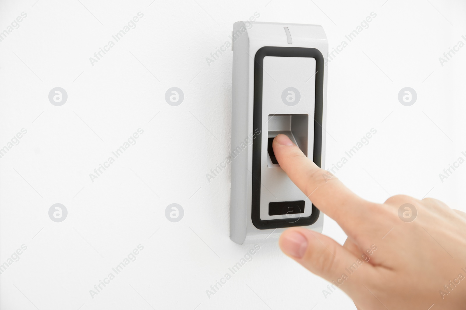 Photo of Young woman pressing fingerprint scanner on alarm system indoors