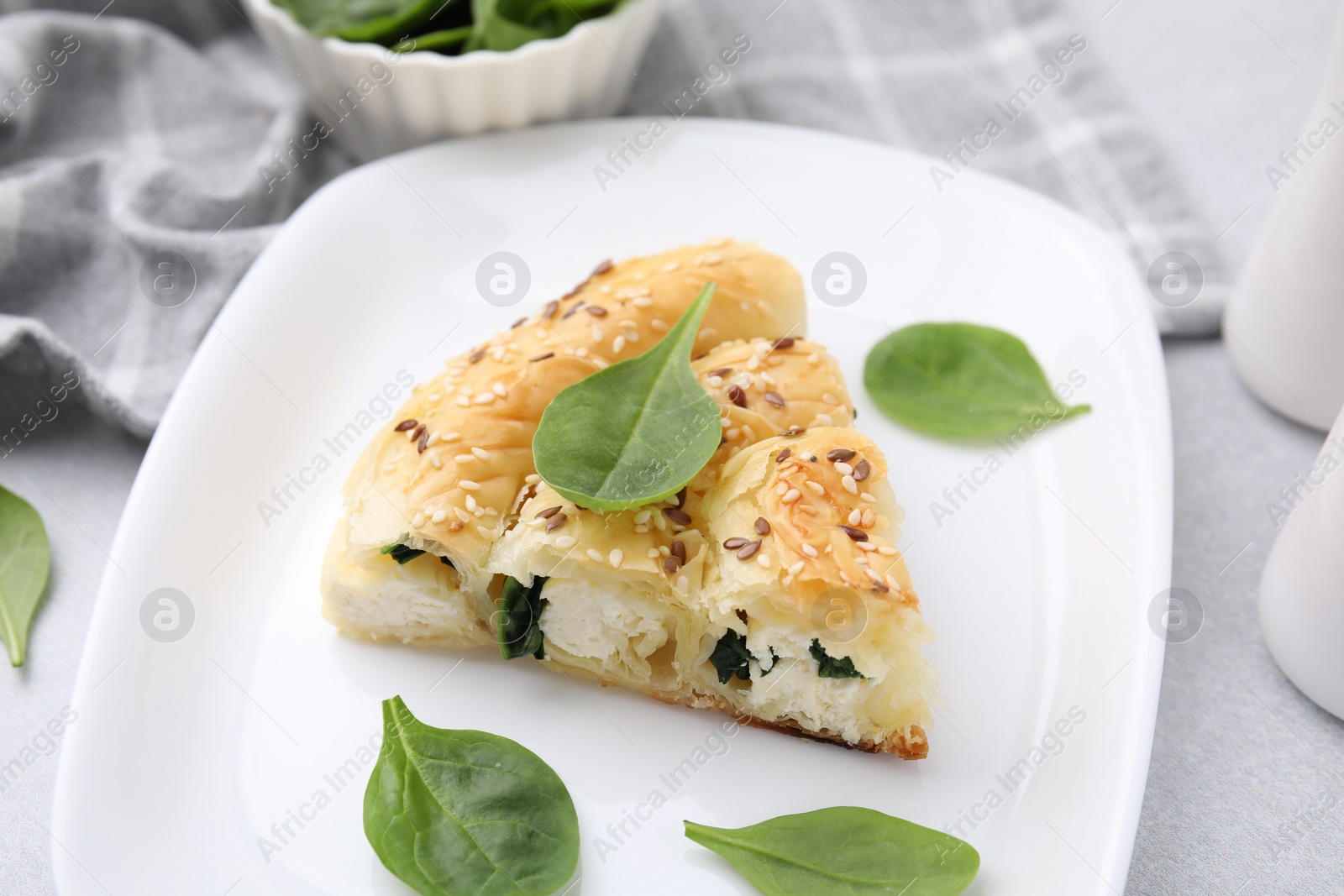 Photo of Piece of delicious puff pastry with spinach on light table, closeup