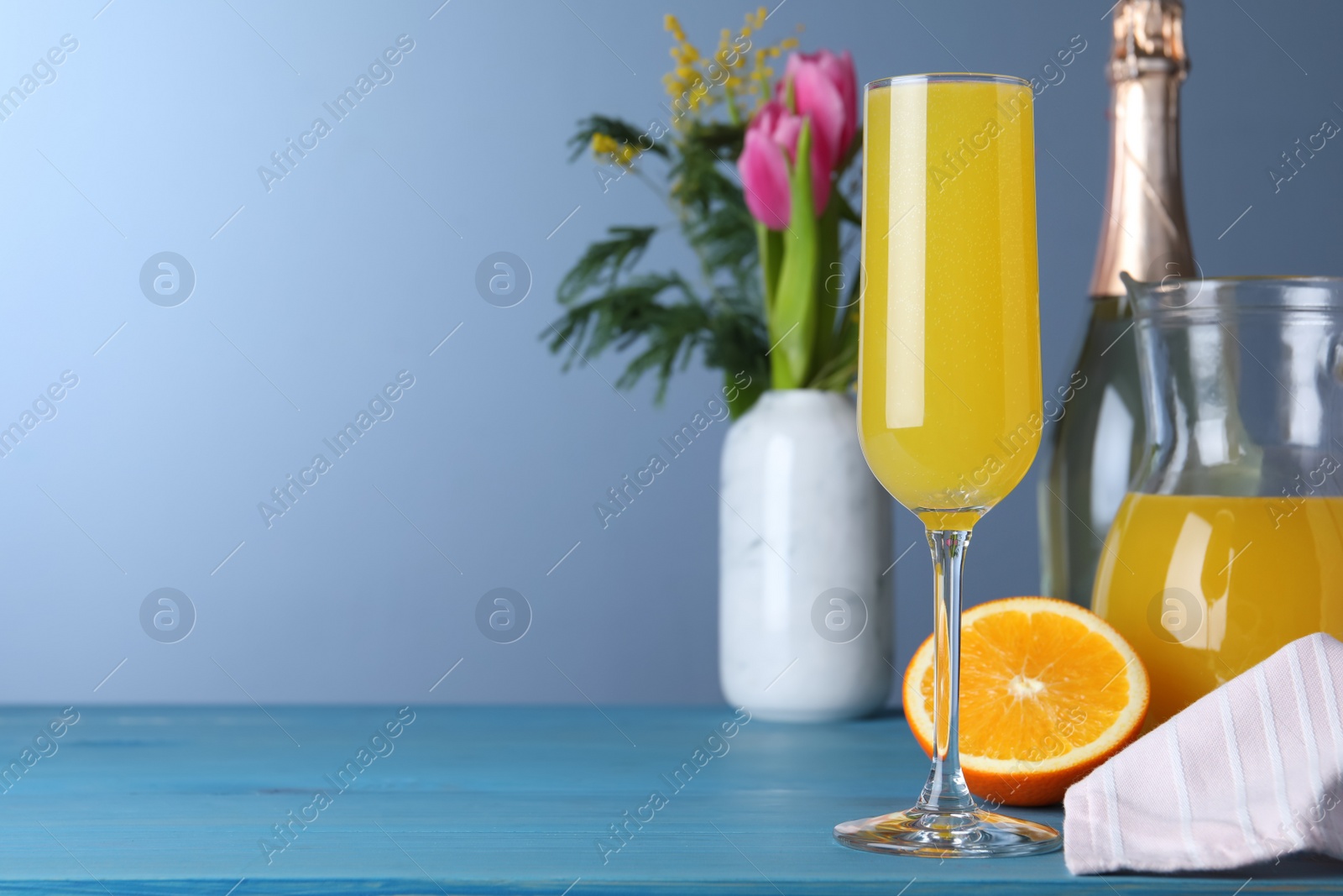 Photo of Glass of Mimosa cocktail on light blue wooden table. Space for text