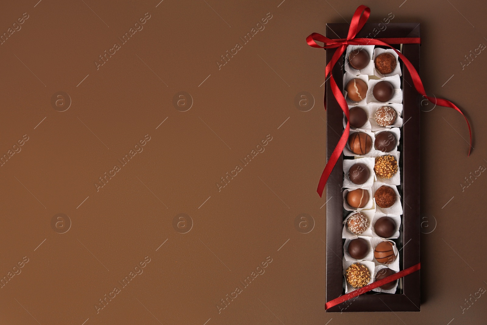 Photo of Box with delicious chocolate candies on brown table, top view. Space for text
