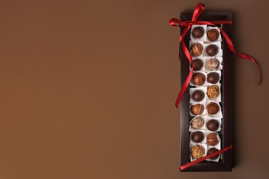 Box with delicious chocolate candies on brown table, top view. Space for text