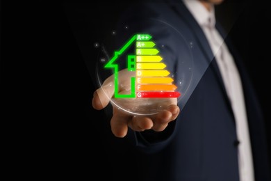 Image of Energy efficiency. Man holding virtual colorful rating against black background, closeup