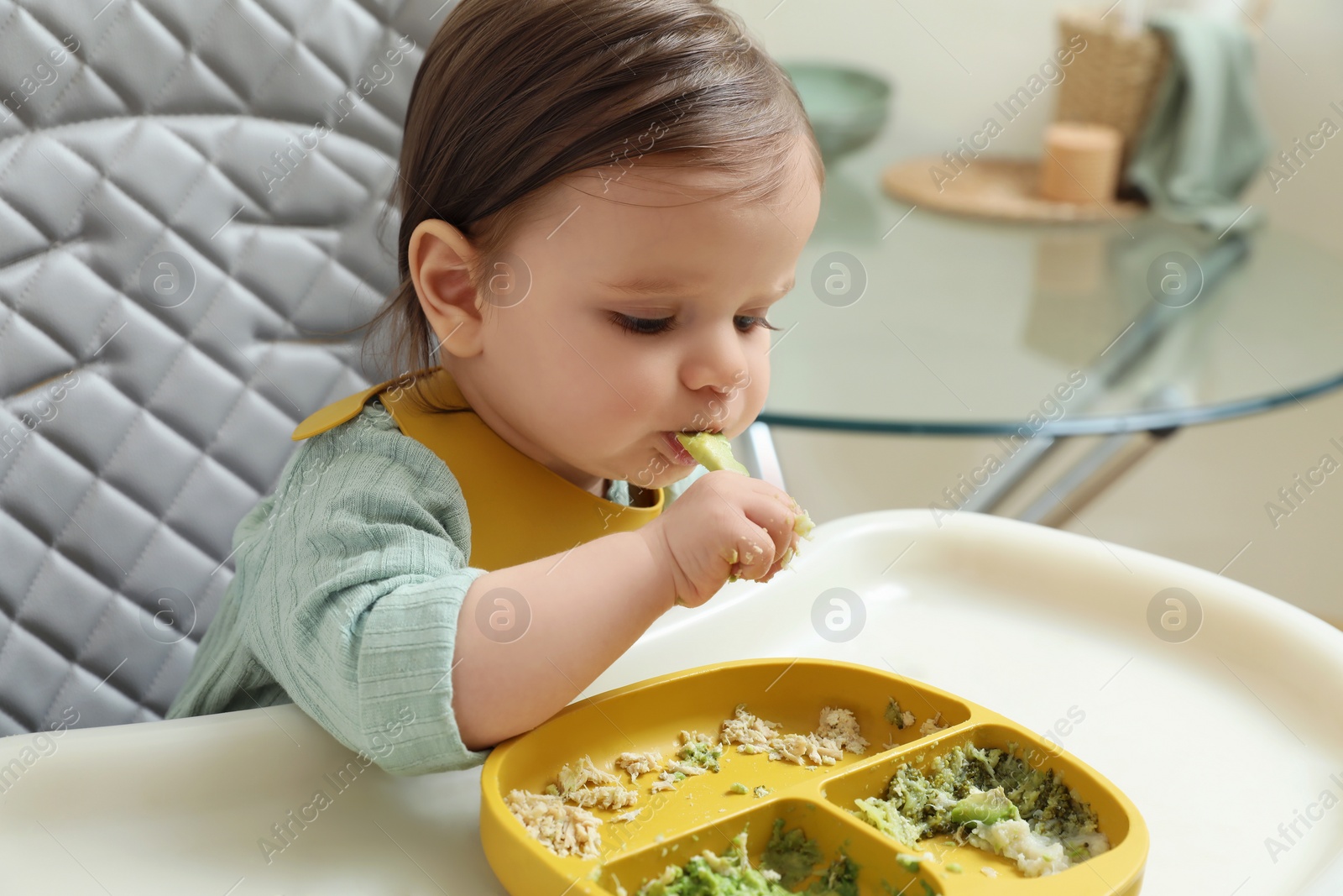 Photo of Cute little baby eating healthy food in high chair indoors