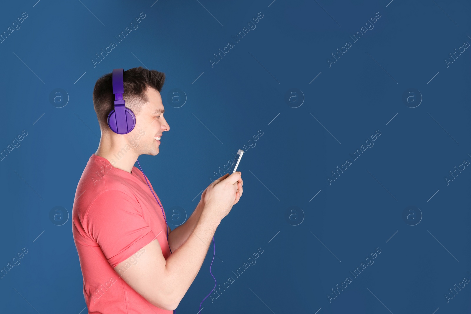 Photo of Man in headphones with mobile device on color background. Space for text