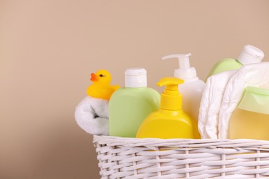 Wicker basket with baby cosmetic products, bath accessories and rubber duck on beige background, closeup