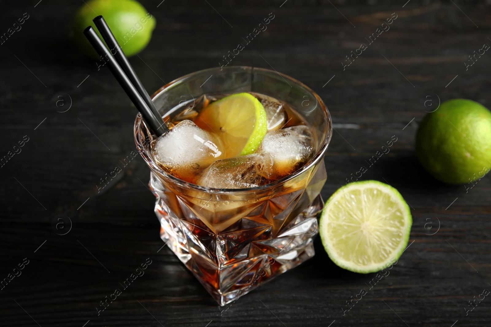 Photo of Glass of cocktail with cola, ice and cut lime on wooden background